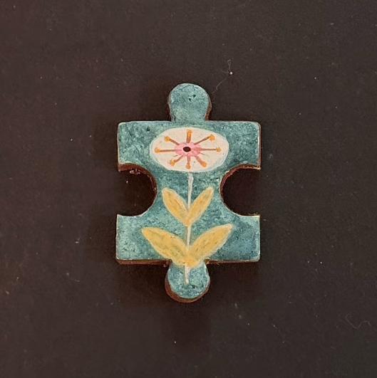Hand-painted clay puzzle magnet with a white flower, pink center, and yellow leaves on a teal background