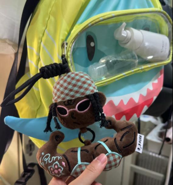 Funny muscle girl plush keychain clipped to a bright green backpack