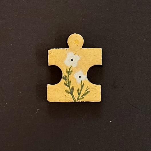 Hand-painted clay puzzle magnet featuring two small white flowers with green stems on a yellow background