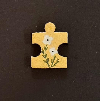 Hand-painted clay puzzle magnet featuring two small white flowers with green stems on a yellow background