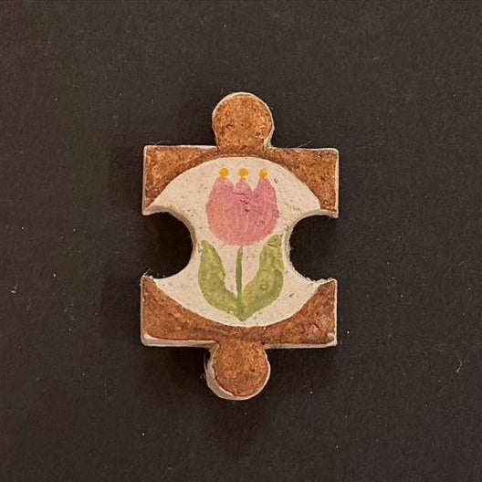 Hand-painted clay puzzle magnet with a pink tulip and green leaves on a warm brown background