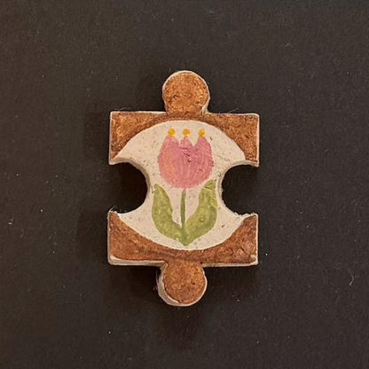 Hand-painted clay puzzle magnet with a pink tulip and green leaves on a warm brown background