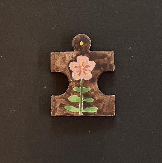 Hand-painted clay puzzle magnet featuring a light pink flower with green leaves on a dark brown background