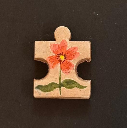 Hand-painted clay puzzle magnet with an orange-red flower and green leaves on a beige background