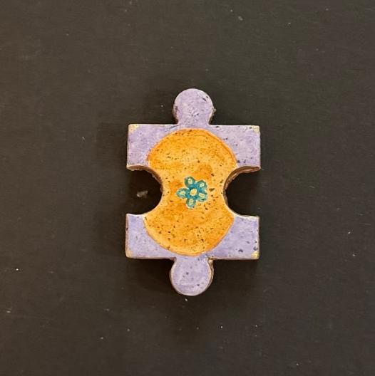 Hand-painted clay puzzle magnet featuring a yellow floral design with a small blue flower on a lavender background