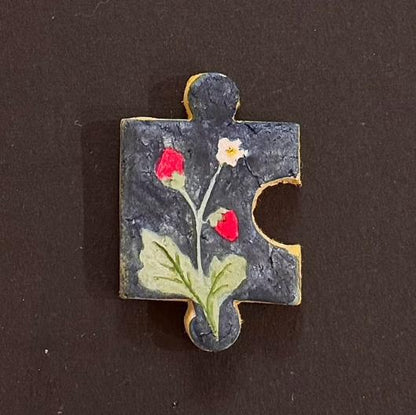 Hand-painted clay puzzle magnet with red flower buds and green leaves on a dark background