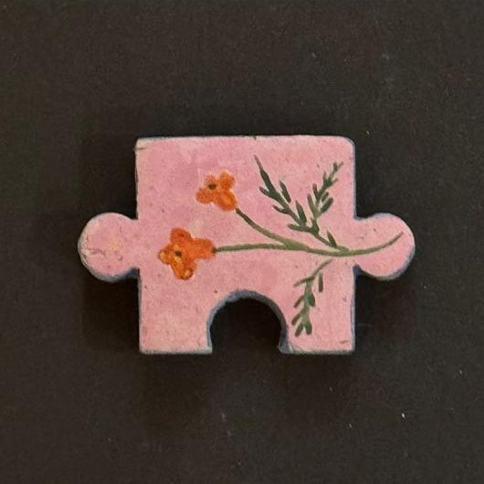 Hand-painted clay puzzle magnet featuring small orange flowers and green branches on a pink background