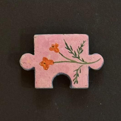 Hand-painted clay puzzle magnet featuring small orange flowers and green branches on a pink background