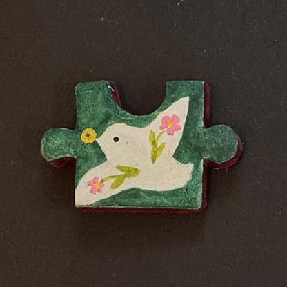 Hand-painted clay puzzle magnet featuring a white bird surrounded by small flowers on a dark green background