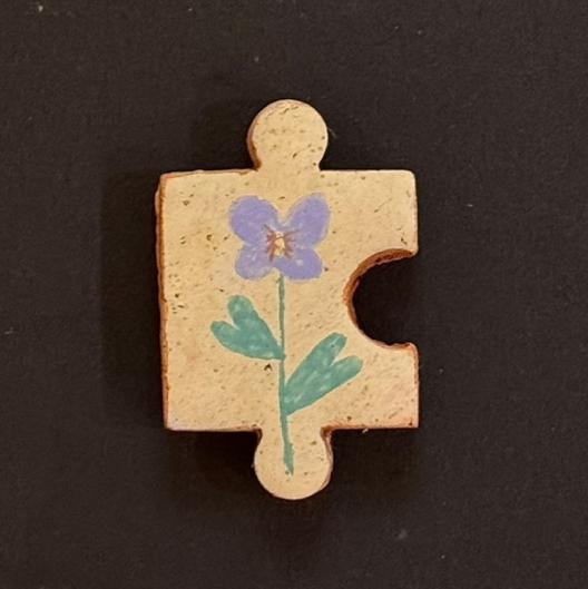Hand-painted clay puzzle magnet featuring a purple flower with green leaves on a light beige background