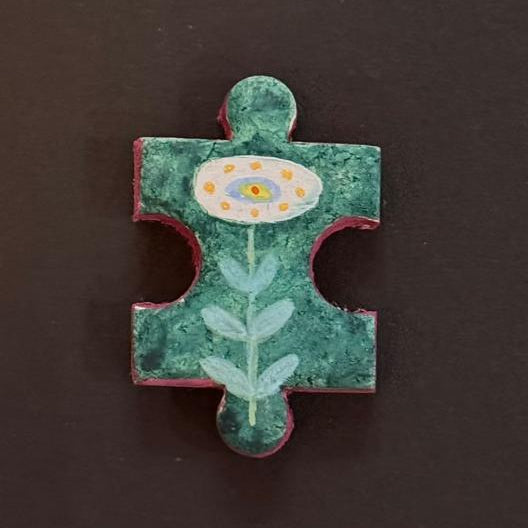 Hand-painted clay puzzle magnet featuring a white flower with yellow details and pale green leaves on a teal green background