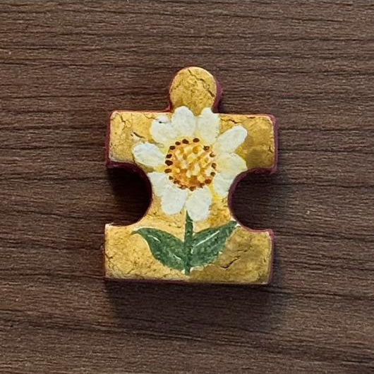 Hand-painted clay puzzle magnet featuring a white daisy with a yellow center and green leaves on a golden yellow background