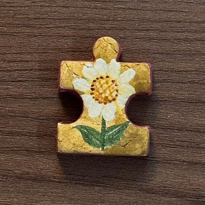 Hand-painted clay puzzle magnet featuring a white daisy with a yellow center and green leaves on a golden yellow background