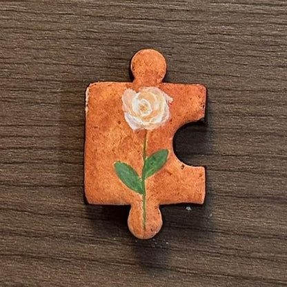 Hand-painted clay puzzle magnet featuring a white rose with green leaves on a warm orange background