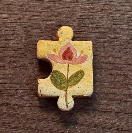 Hand-painted clay puzzle magnet featuring a red flower with green leaves on a pale yellow background