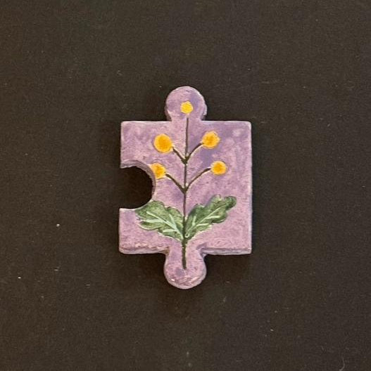 Hand-painted clay puzzle magnet featuring small yellow flowers and green leaves on a lavender background