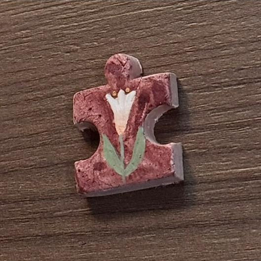 Hand-painted clay puzzle magnet featuring a white flower with green leaves on a burgundy background