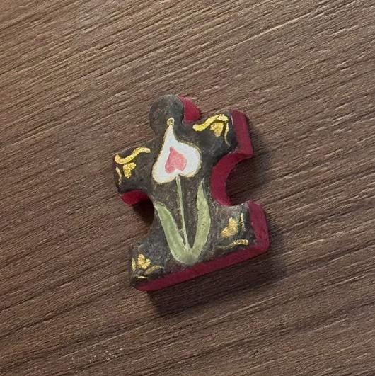 Hand-painted clay puzzle magnet featuring a white flower with red details and green leaves on a dark background