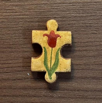 Hand-painted clay puzzle magnet featuring a red flower with long green leaves on a golden yellow background