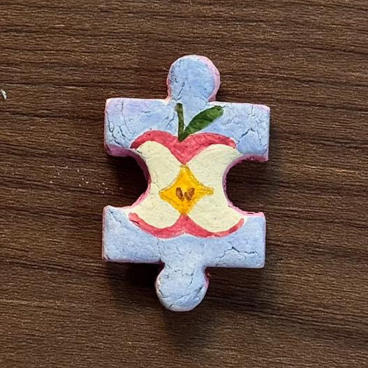 Hand-painted clay puzzle magnet featuring a colorful apple cross-section with a yellow center on a light blue background