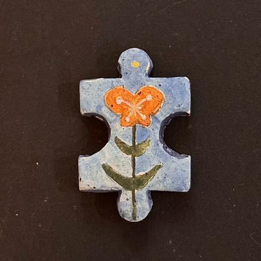 Hand-painted clay puzzle magnet with an orange flower and green stem on a light blue background