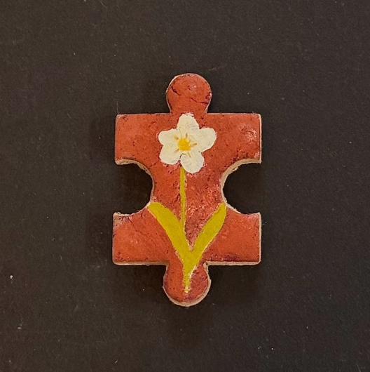 Hand-painted clay puzzle magnet with a white flower and yellow stem on a warm orange background