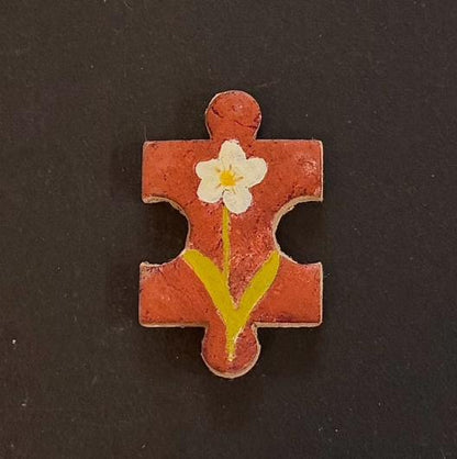 Hand-painted clay puzzle magnet with a white flower and yellow stem on a warm orange background