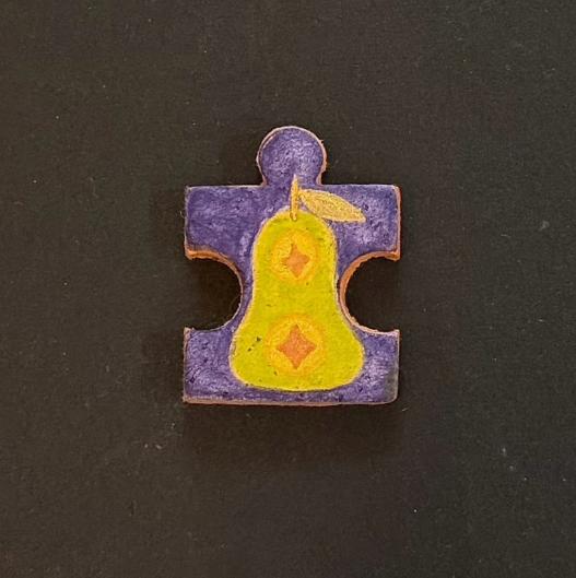 Hand-painted clay puzzle magnet featuring a yellow pear with orange details on a purple background