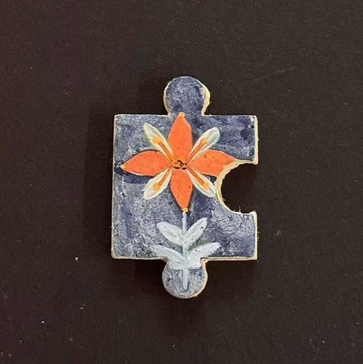 Hand-painted clay puzzle magnet with orange and white flowers on a dark blue background