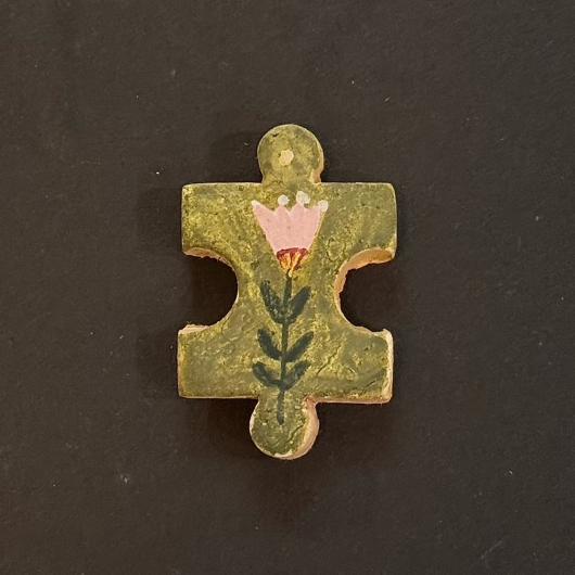 Hand-painted clay puzzle magnet featuring a pink flower with green leaves on an olive green background