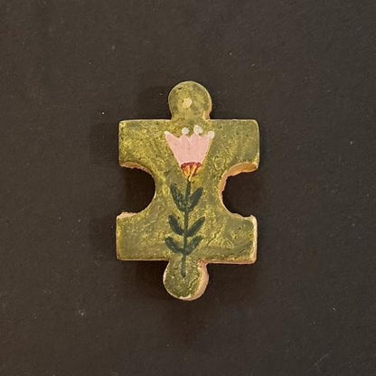Hand-painted clay puzzle magnet featuring a pink flower with green leaves on an olive green background