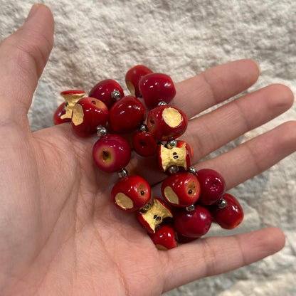 Red apple and bitten apple core beads displayed in an open palm