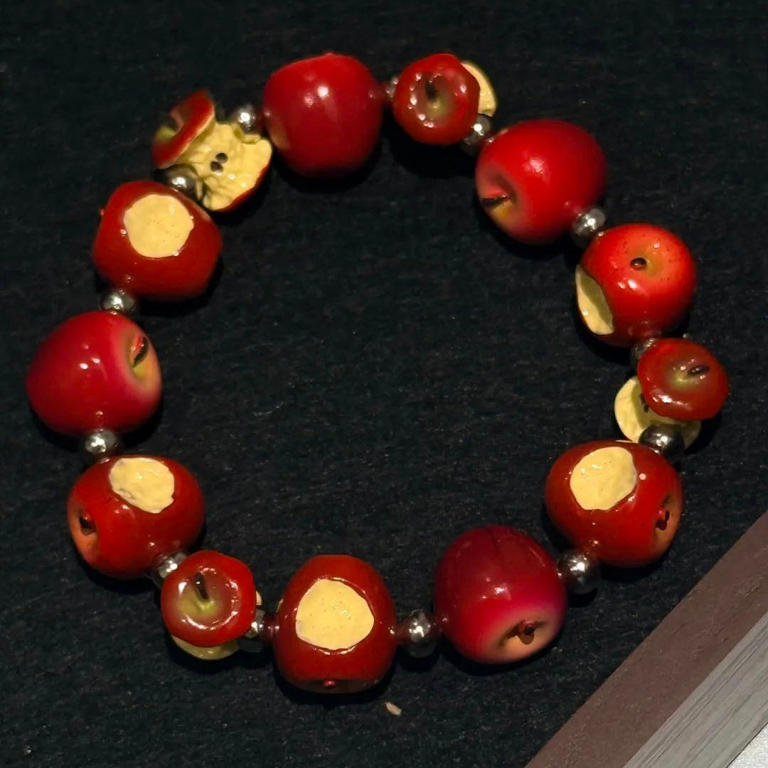 Apple core bracelet arranged in a circle on a black background, showing red apple beads and silver-tone spacers