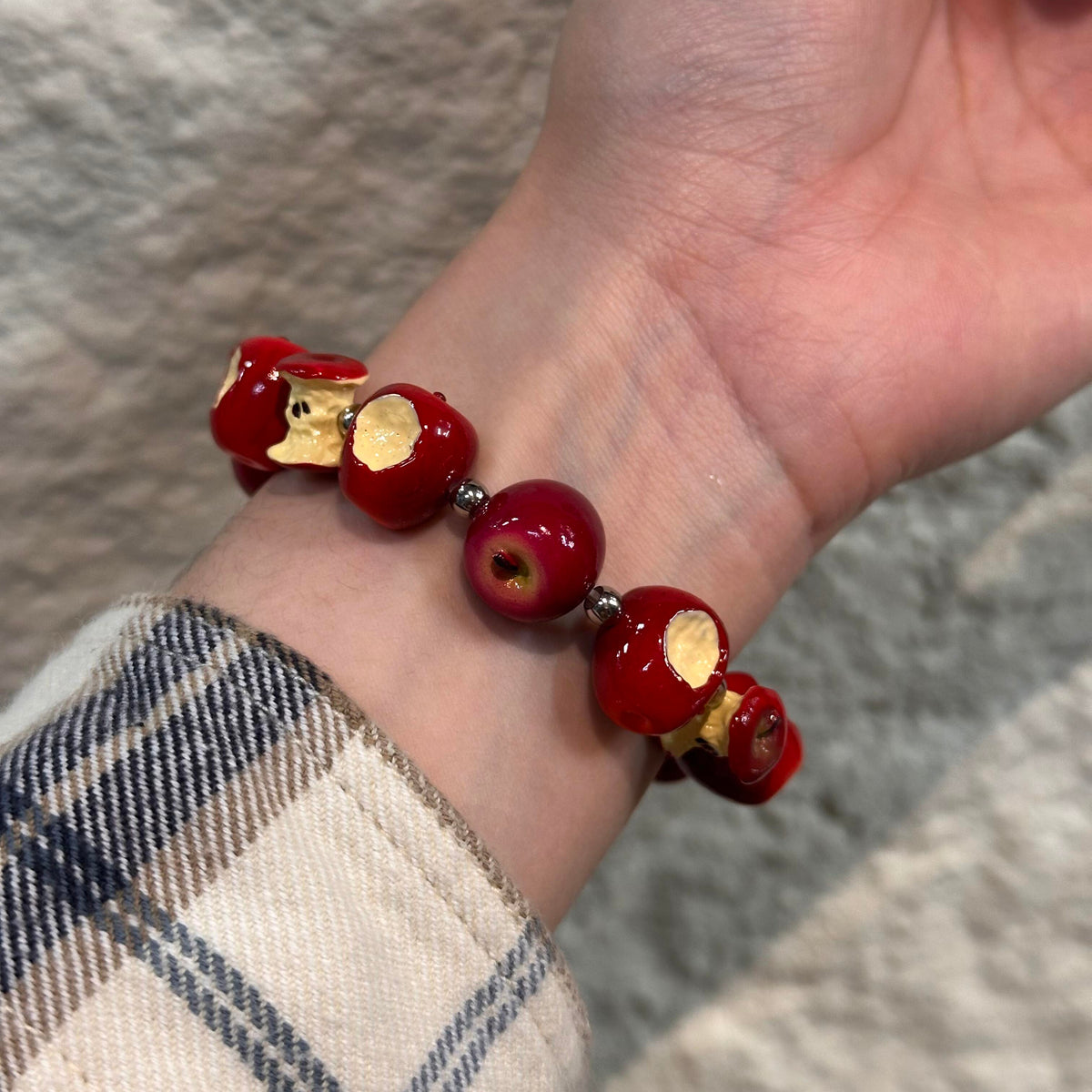 Red apple and bitten apple core bracelet worn on a wrist with a plaid sleeve