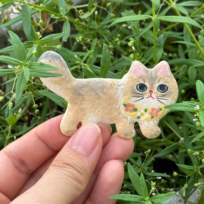 Hand holding a light-colored ceramic cat magnet with painted details outdoors
