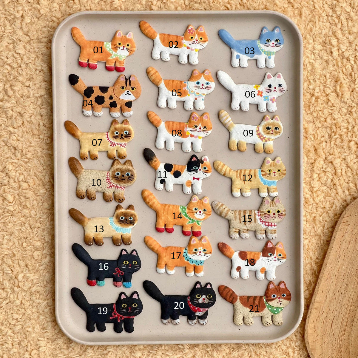 Assorted ceramic cat fridge magnets in different colors and patterns displayed together on a tray