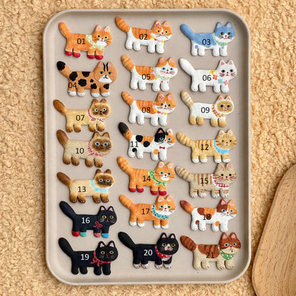 Assorted ceramic cat fridge magnets in different colors and patterns displayed together on a tray