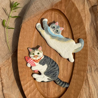 Two colorful ceramic cat fridge magnets displayed on a wooden surface