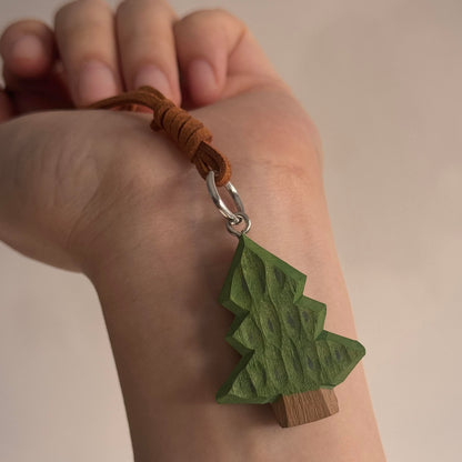 Hand holding a miniature green wooden Christmas tree charm with hanging strap