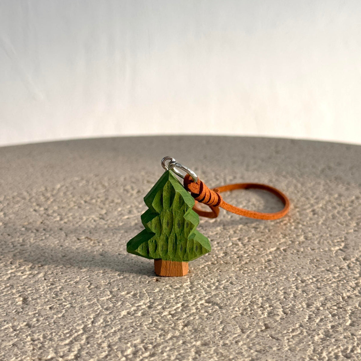 Mini green wooden Christmas tree hanging charm with brown strap displayed on a light surface