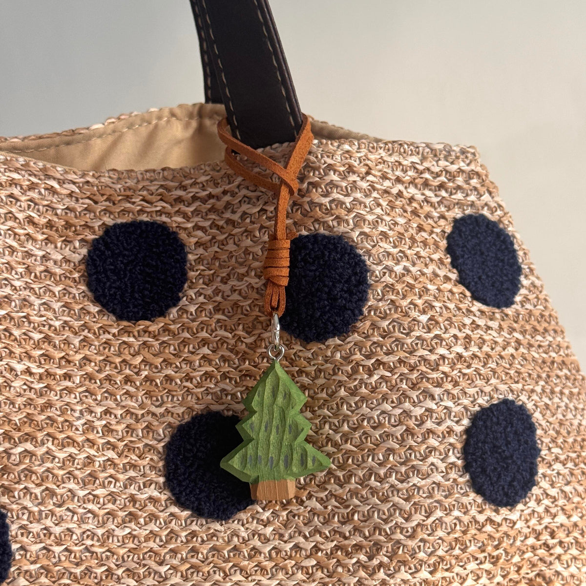 Mini wooden Christmas tree charm attached to a beige woven bag with dark polka dots