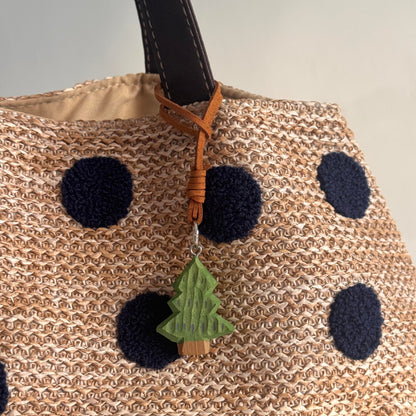 Mini wooden Christmas tree charm attached to a beige woven bag with dark polka dots