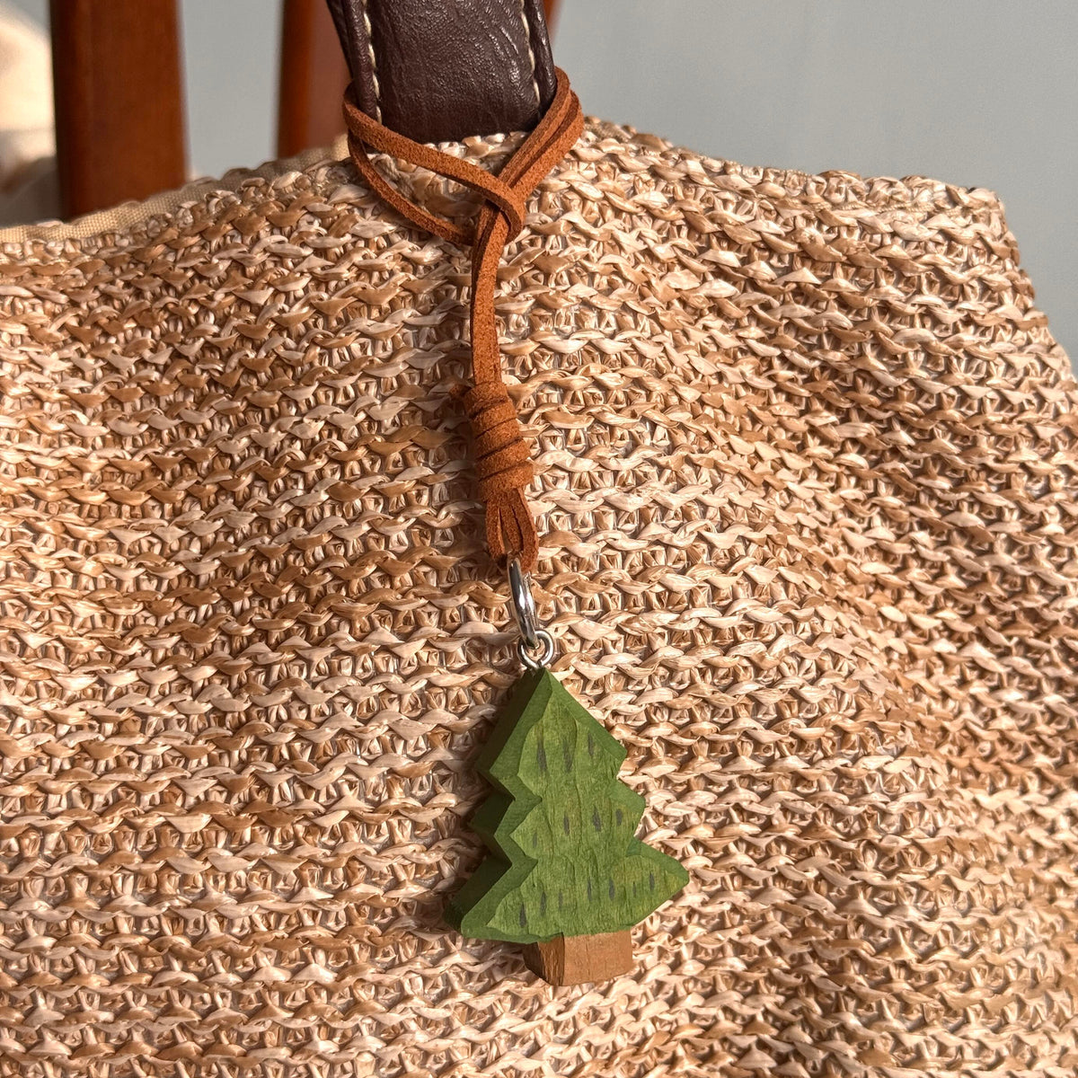 Green wooden Christmas tree charm hanging from a woven bag with brown strap