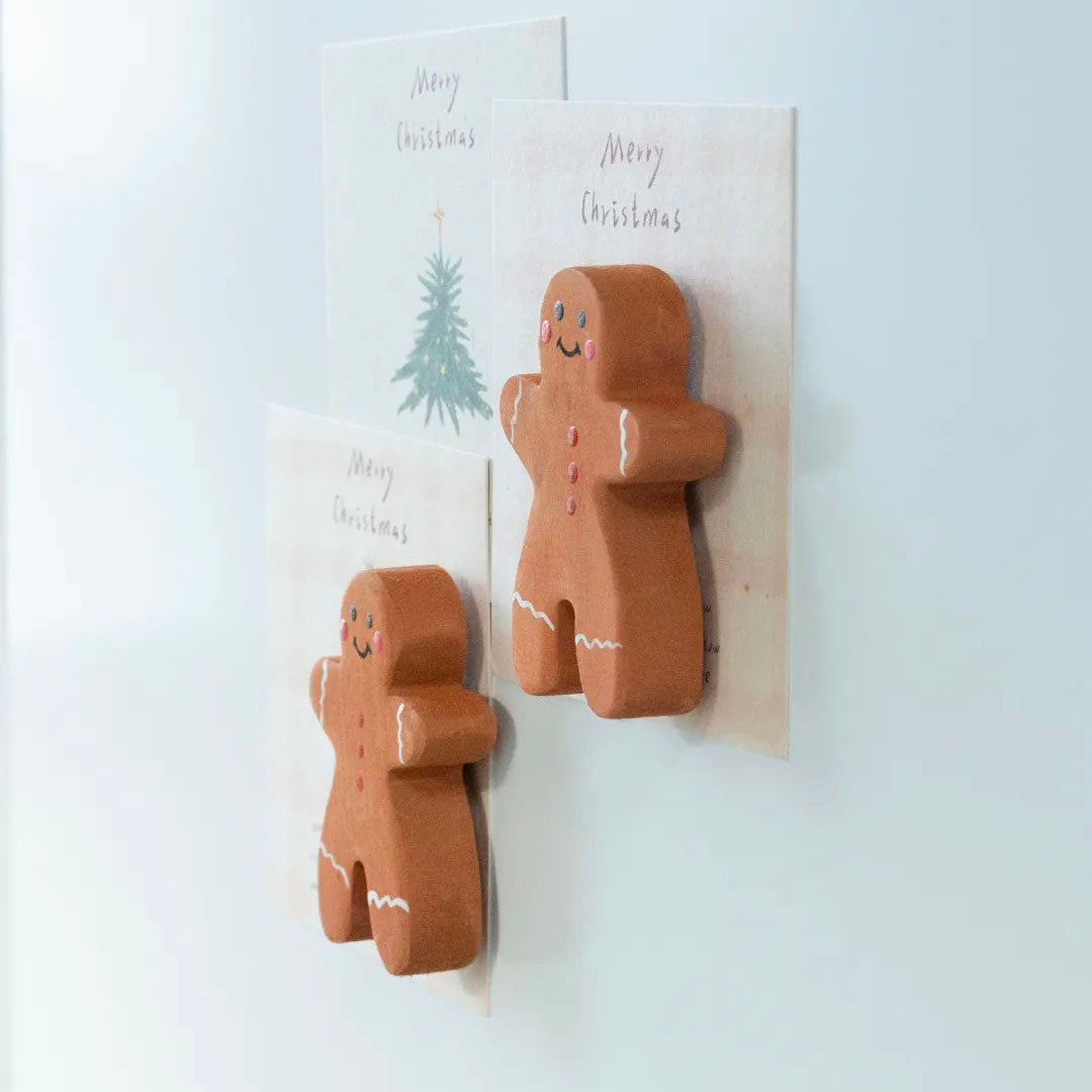 Side view of two wooden gingerbread man magnets showing their carved thickness