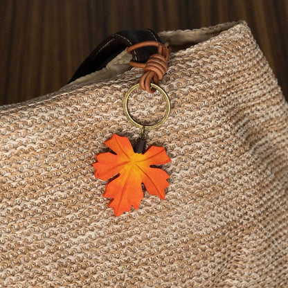 Hand holding an orange wooden maple leaf charm with a brown hanging strap