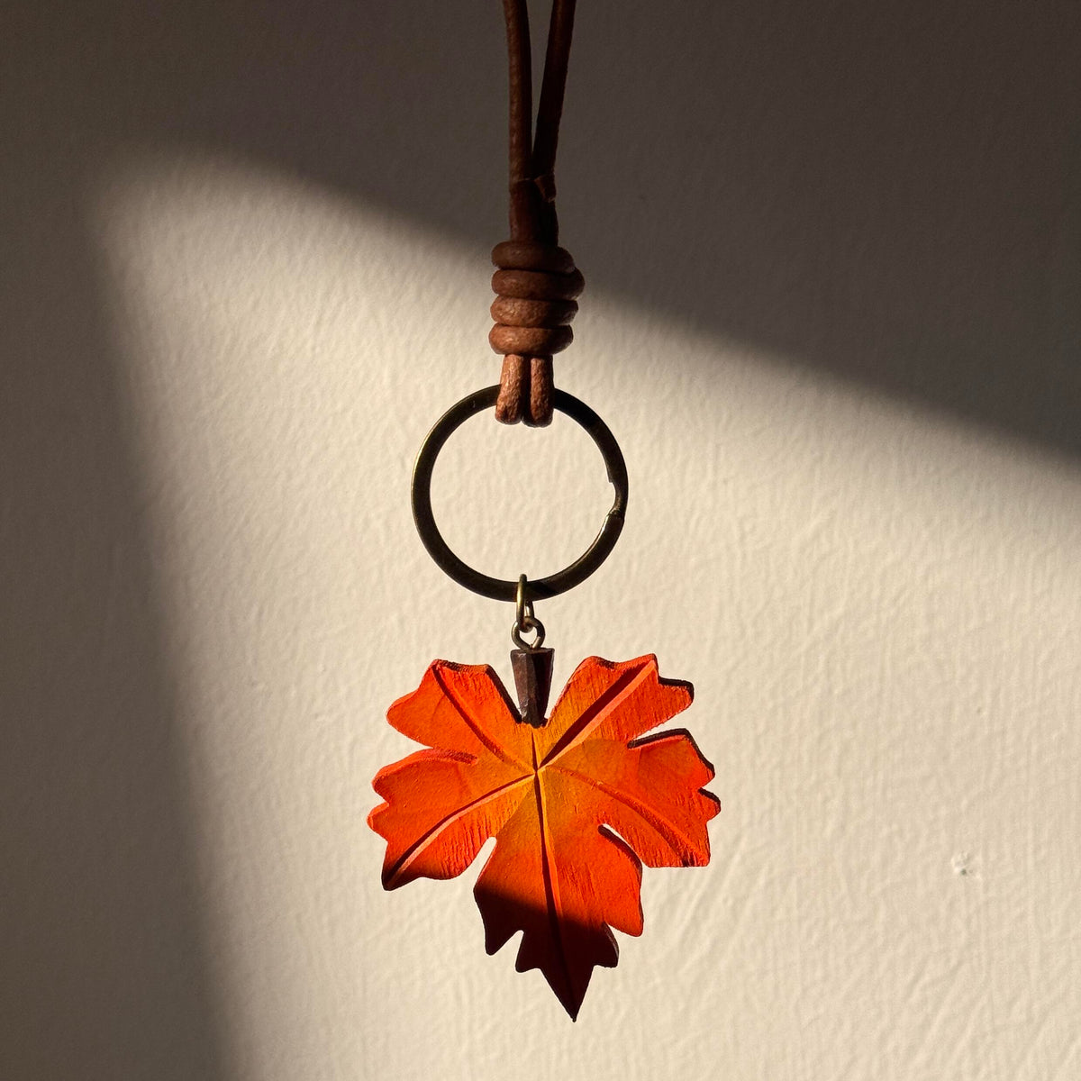 Hand-carved orange wooden maple leaf charm hanging in warm natural light
