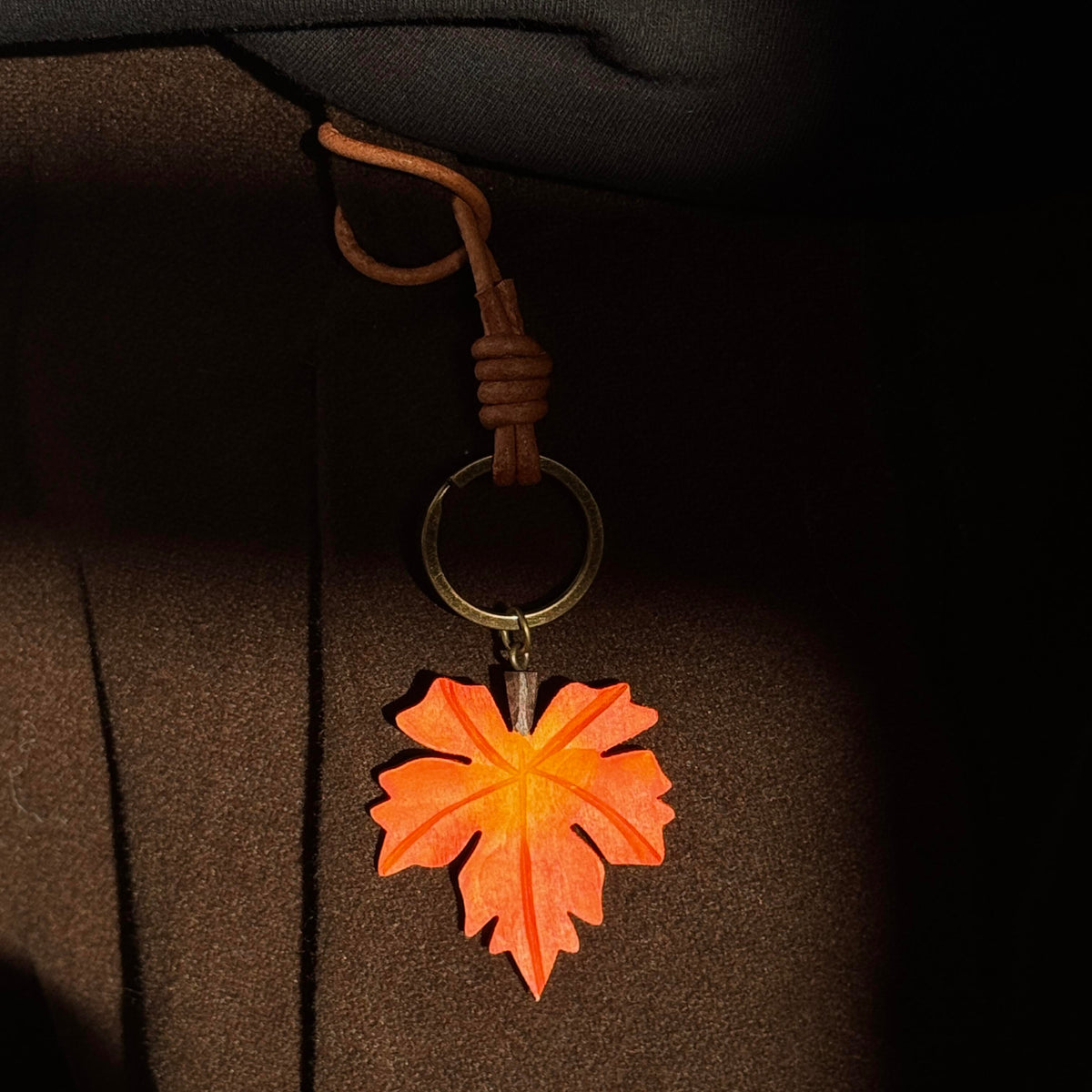 Orange wooden maple leaf charm hanging from a light-colored bag with a brown strap