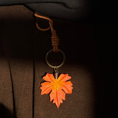 Orange wooden maple leaf charm hanging from a light-colored bag with a brown strap
