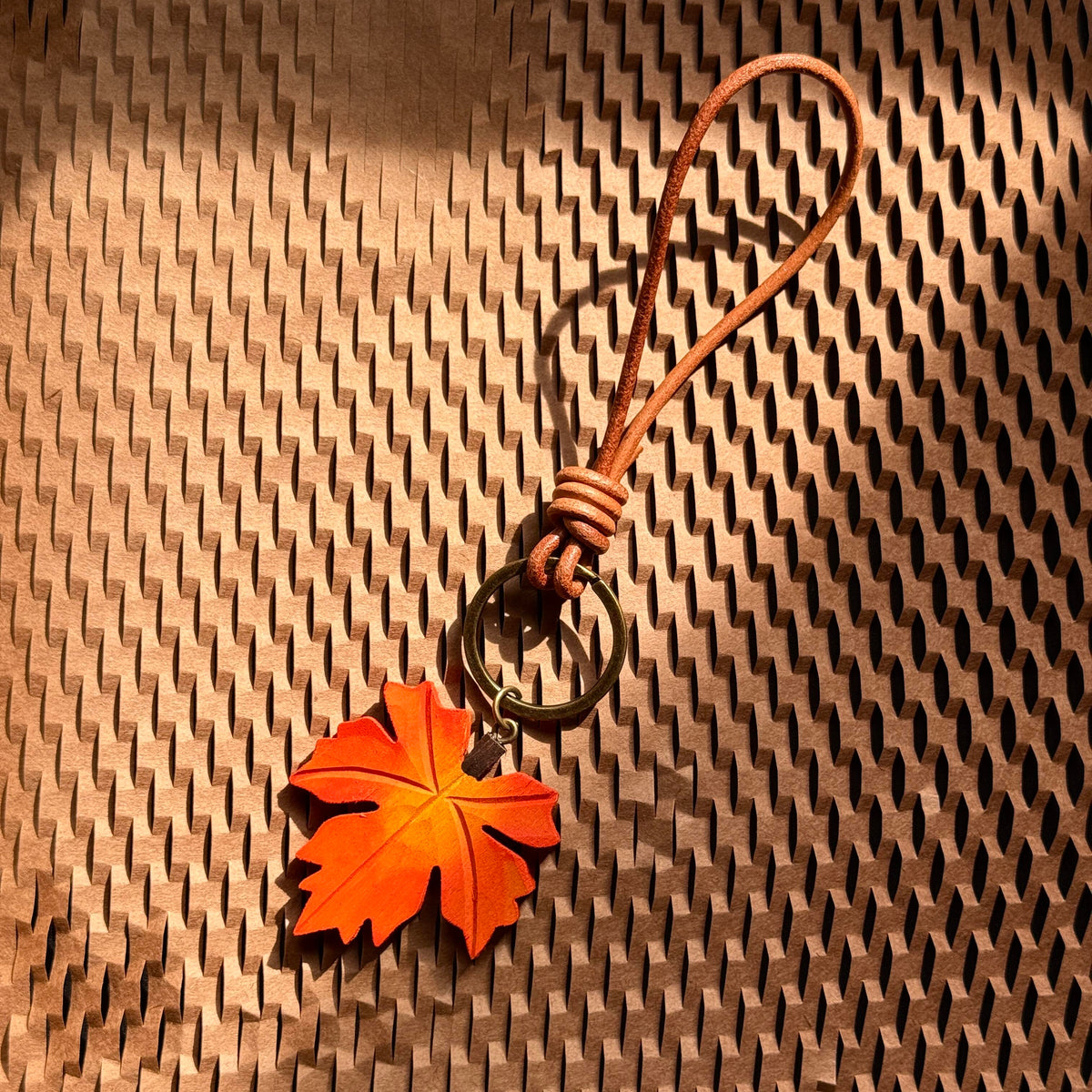 Orange wooden maple leaf hanging charm with brown strap displayed on a woven surface