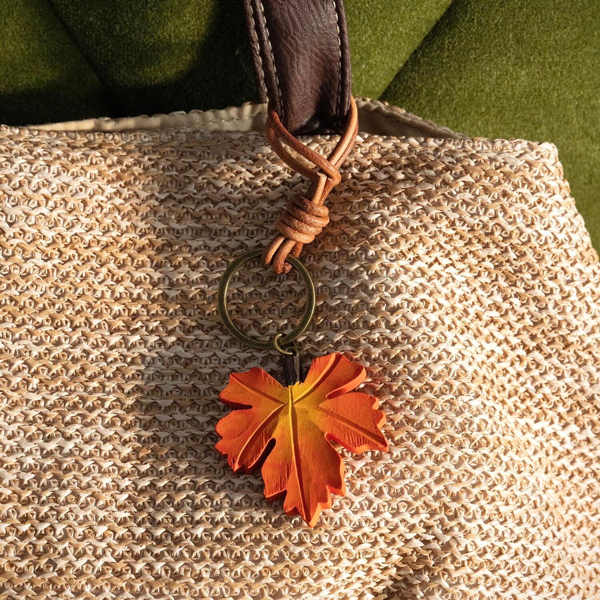 Hand-carved orange wooden maple leaf charm hanging from a woven bag with a brown strap
